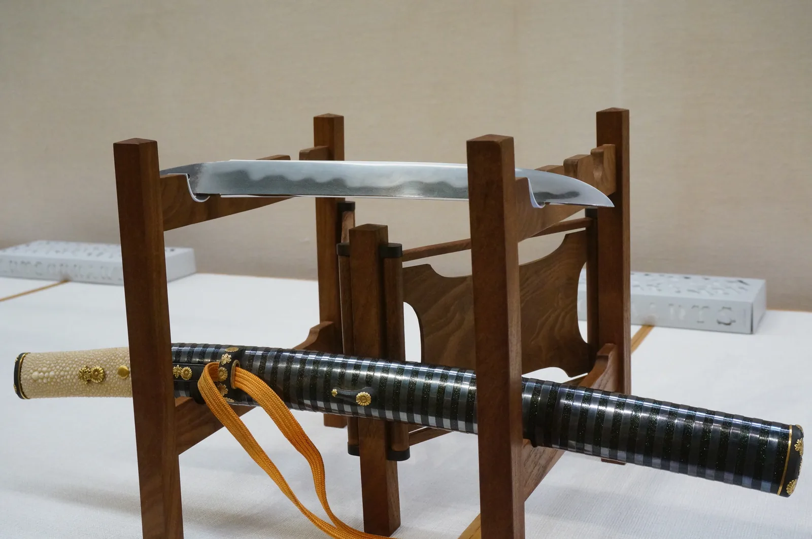 Hoja de tantō sobre un soporte, con su montura de empuñadura de marfil junto a ella.