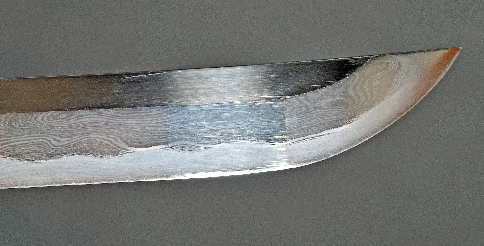 Fotografía macro de la punta de una katana: se ve la línea del yokote, la hoja de acero plegado con su hada visible, y el hamon entrando en el kissaki y volviendo sobre sí mismo (kaeri).