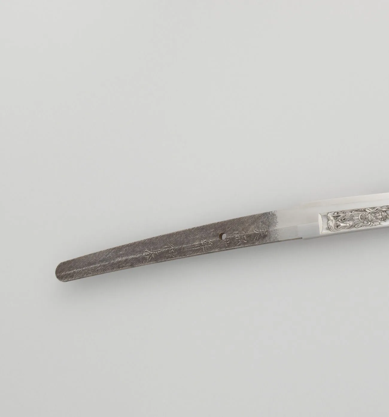 Fotografía de una espiga (nakago) de una katana japonesa antigua: se ven el limado diagonal (yasurime), un orificio (mekugi-ana), varios caracteres grabados y el extremo redondeado (nakago-jiri).