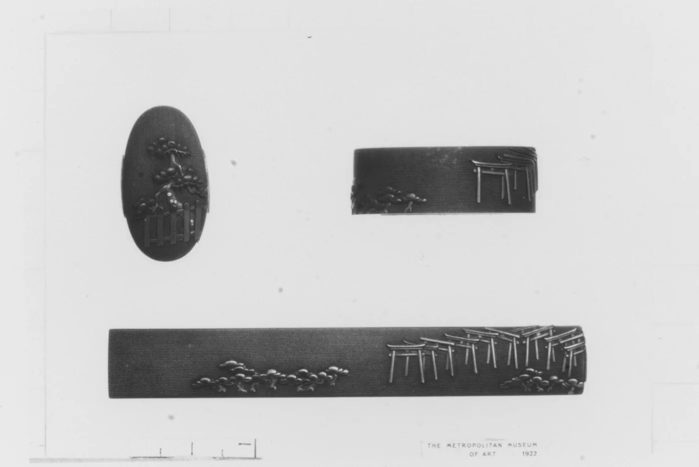 Juego de fuchi y kashira con relieve de pinos y toriis, y la empuñadura montada abajo mostrando el conjunto completo.