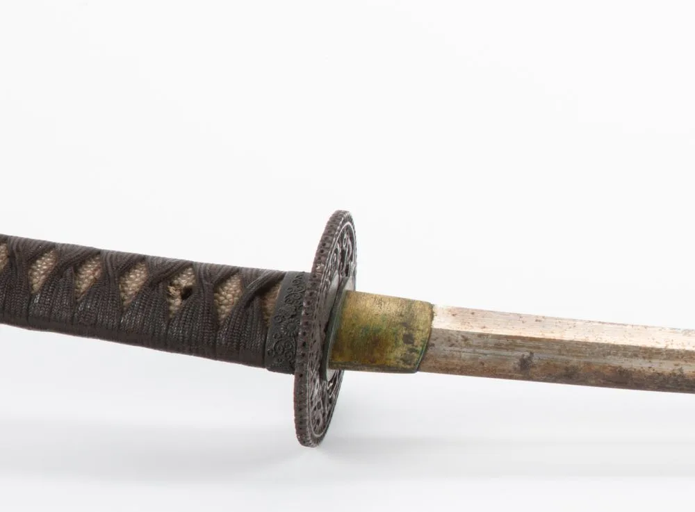 Detalle de una espiga desnuda con su habaki de latón, la tsuba y el fuchi, mostrando cómo el collar calza justo sobre el filo.