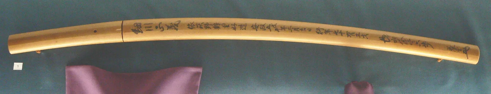 Vaina de madera clara con una inscripción de sayagaki en tinta a lo largo del canto.